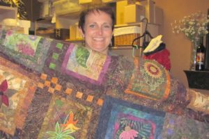 Carrie Schulstad shows off one of the many intricate quilts currently filling the back room of her store, The Uncommon Gift.