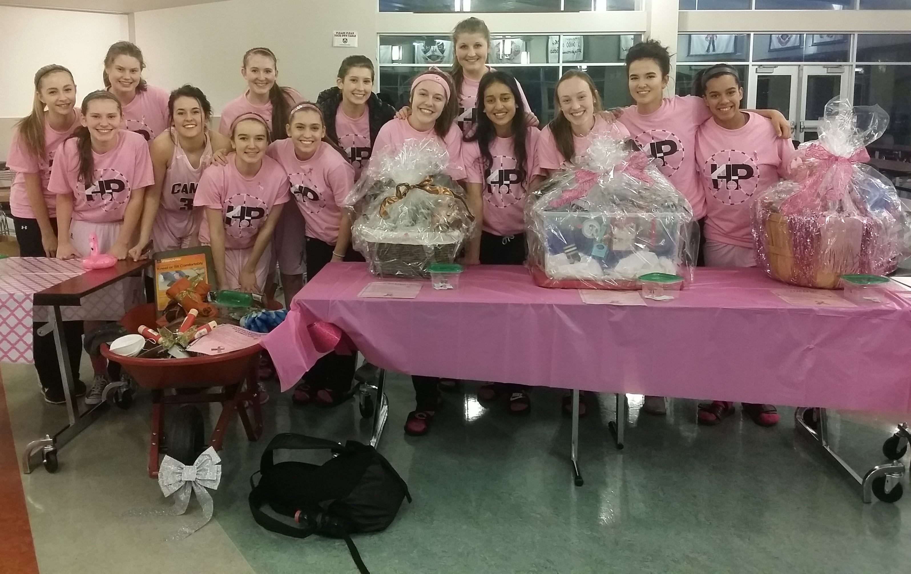 The Camas High School basketball team gathers around Hoops of Pink baskets.