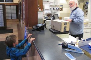 Dan Smith talks with the son of one of his postal customers, at the post office, in downtown Camas. Smith has collected several wind-up toys to show to children. He has worked for the United States Postal Service for 33 years, in the local office.