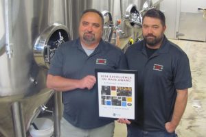 Mill City Brew Werks owner Mark Zech (left) and General Manager/Brewer Chris Daniels (right) stand with an Excellence on Main award from the Washington State Main Street Program. Downtown Camas Association Executive Director Carrie Schulstad, Board President Caroline Mercury and Vice President/Treasurer Dawn White accepted the Economic Vitality honor, on behalf of Mill City, Wednesday, during the State Preservation and Main Street Conference, in Wenatchee.