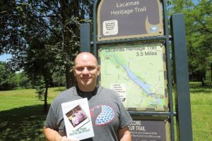 Dale Rule holds up a copy of his book, "Is the Prize Worth the Price?," after walking the Lacamas Heritage Trail. The 43-year-old said he has been on this stretch so many times, he could probably walk it blindfolded "without falling into the lake, hitting a tree or getting lost."