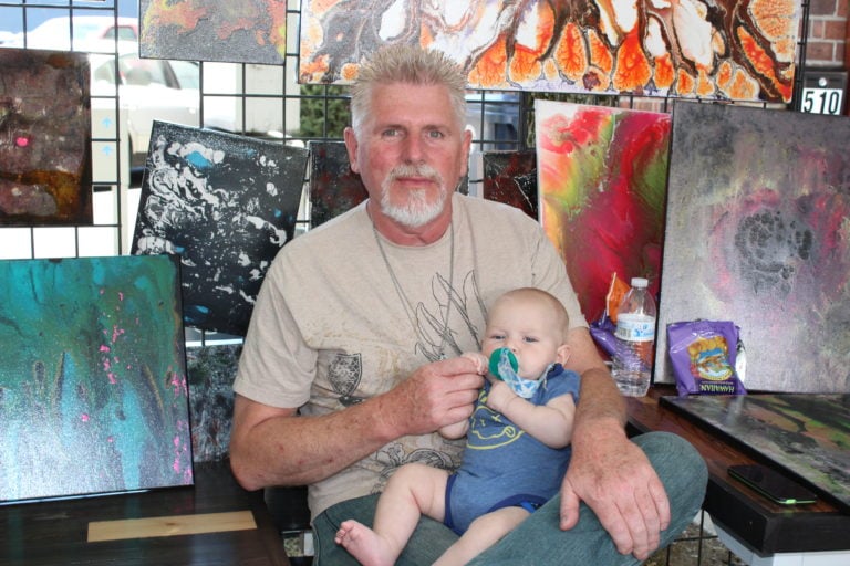 Artist Scott Hampel, of the Vancouver-based Copperedge Studio, enjoys Camas Days with his 5-month-old grandson, Ryder, on Friday, July 21.