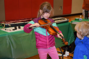 Emily Lampmann, a first-grader at Hathaway Elementary School, plays a violin provided by Opus School of Music, during her school's Dec. 6 Dream Big event, while her younger brother, Alexander Lampmann, watches.