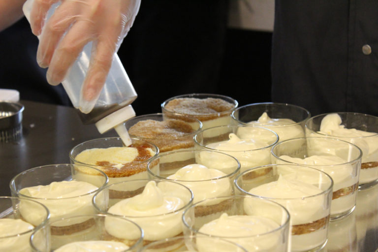 Advanced culinary students from Washougal and Excelsior high schools drizzle almond-flavored espresso on top of a sponge cake, to create traditional tiramisu flavors.