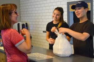 Longtime Hana Foods patron Sheryl Obegi (left) accepts her to-go order from Hana servers Sophie Eagle (center) and Eric Park (right) on the restaurant's re-opening day, Monday, June 25.