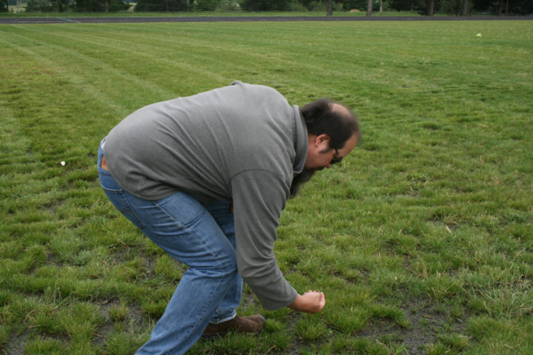 Eighth grade science teacher Brett Cox picks up a sharp shard of plastic on the new football field at Jemtegaard Middle School in Washougal.