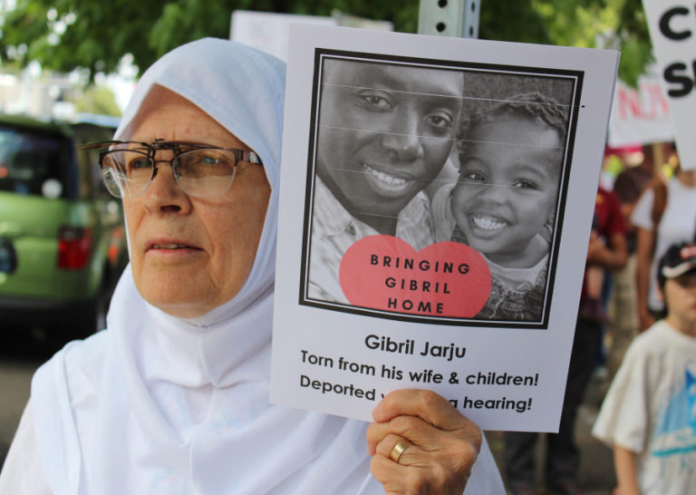 Beth Sermet, of Vancouver, holds a sign showing Gibril Jarju, an immigrant she says was taken from his Vancouver home and family in February and deported within weeks with no hearing.