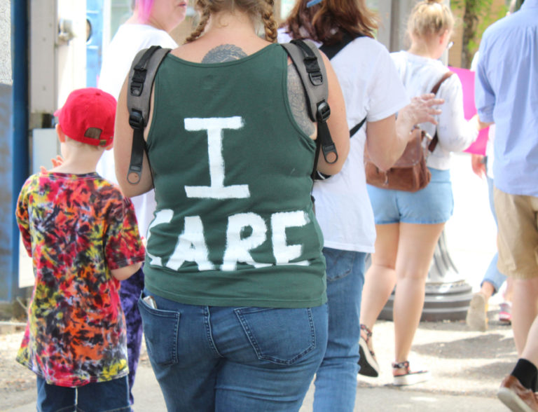 A woman wears an "I Care" shirt at the June 30 Families Belong Together march in Vancouver in response to a jacket stating, "I really don't care.
