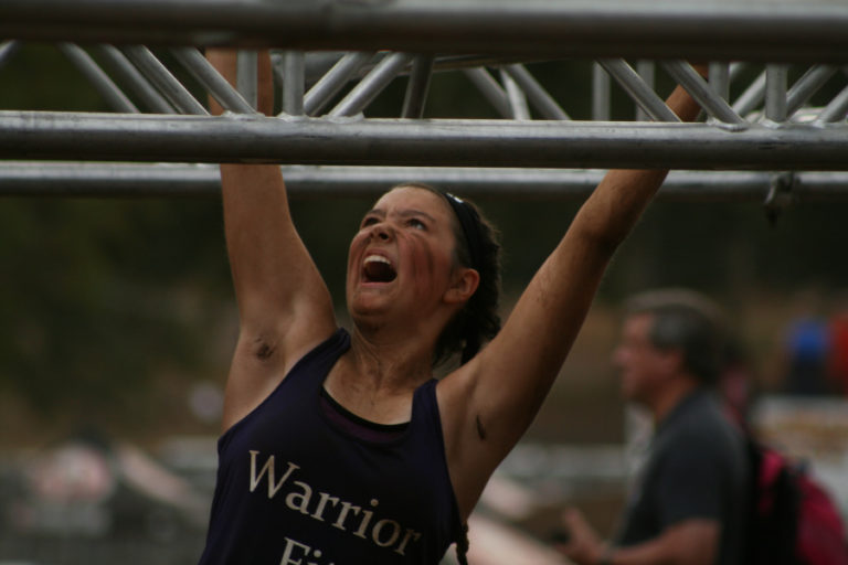 A Spartan racer shows grit on the monkey bars, fighting to keep a grip, a challenging feat especially when your hands are covered in mud.