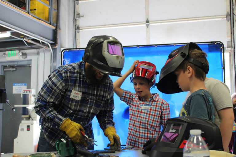 SIGMADESIGN welder Ryan Zahniser (left) gives a welding demonstration to several SIGMADESIGN employees&#039; children, including Parker Irvine, 9, (center) and Jameson Baerwaldt (right) on April 25.