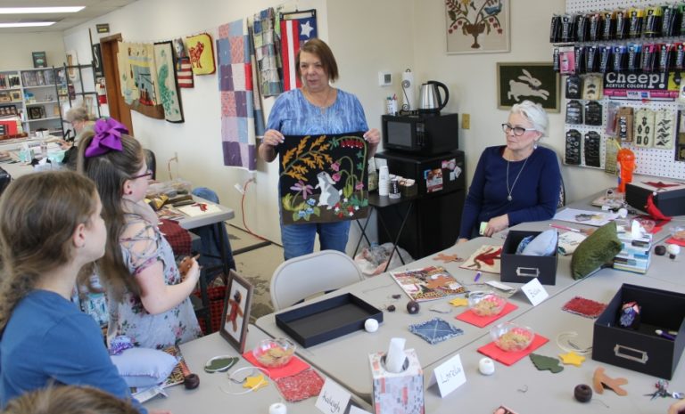 Camas resident Kathy Begier shows off her latest wool applique project to Anna Davis (right) and members of the "applique club" at A Place to Create in Washougal.