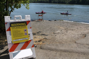 Kayakers paddle on Lacamas Lake near a "Warning: Toxic Algae Present" sign posted at the boat launch off Leadbetter Road on Friday, July 31. Despite public health department warnings asking people to refrain from swimming in the water, hundreds of users have flocked to the lake during the recent stretch of warm weather. (Kelly Moyer/Post-Record)