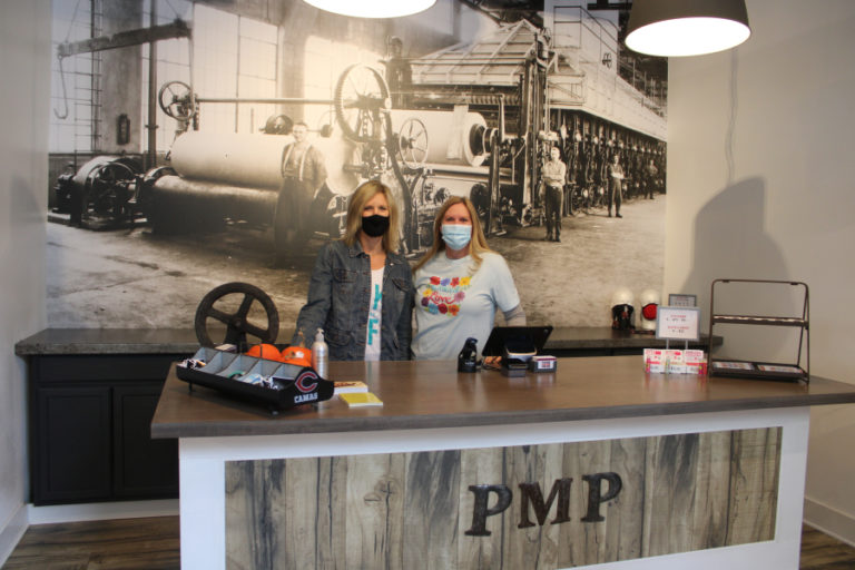 Papermaker Pride employee Kris Blair (left) and co-owner Karen Gibson (right) stand in front of a photo of Camas' historic paper mill inside the retail shop's new space, at 339 N.E. Fourth Ave., in downtown Camas, on Thursday, Oct.