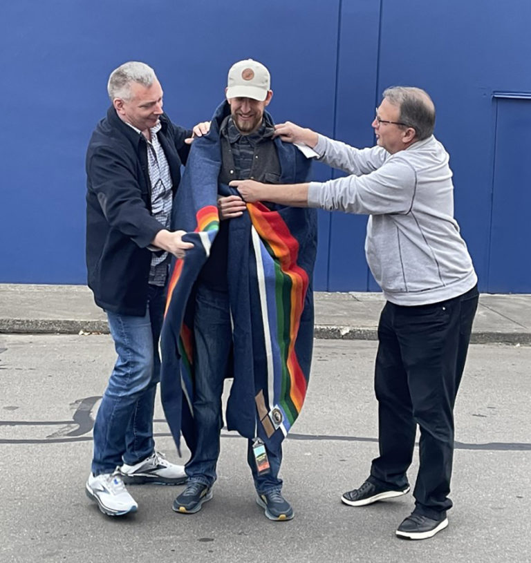 Washougal artist Travis London (center) receives a blanket from Pendleton Woolen Mills employees during a dedication ceremony on Monday, Nov.
