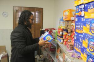 Reuben Cottingham, Akin’s East County Family Resource Center manager, picks up a box of graham crackers from the food shelves at the center on Oct. 28, 2024. Cottingham said the food pictured above, which is intended for the Washougal School District’s backpack program, “will be gone within two weeks.” (Doug Flanagan/Post-Record)