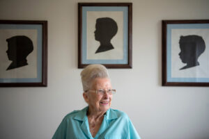 Camas historian Virginia Warren sits on her bed in April 2019 below three silhouettes she traced and cut out of her sons more than 50 years ago. (Alisha Jucevic/The Columbian files)