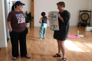 Camas Pride Committee chairs Brie Hilliard, left, and Jacquie Hill discuss the 2025 Camas Pride block party poster inside LiveWell Camas on May 8, as Emma Hilliard, 11, runs past them. (Kelly Moyer/Post-Record)