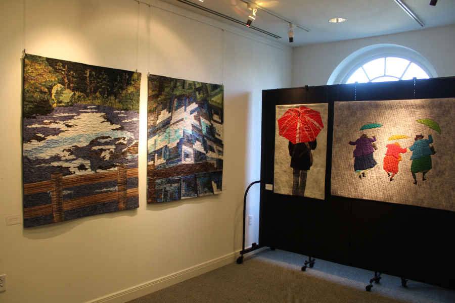 Four art quilts hang inside the Second Story Gallery on Friday, June 6, 2025. Part of the gallery’s monthlong Storyteller Quilters’ art show, the pieces include, from left, “Wizard Falls” and “Blues of Metolius” by artist Gerrie Thompson and “Red Umbrella” and “Puddle Jumpers” by artist CarolAnne Olson. (Photos by Kelly Moyer/Post-Record)