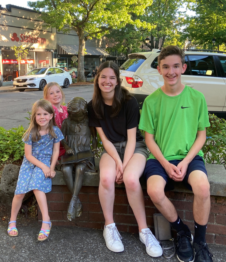 The grandchildren of Camas Downtown Association board member Randy Curtis pose for a photo with the Little Bronze Girl statue in downtown Camas in 2021. (Contributed by the Downtown Camas Association)