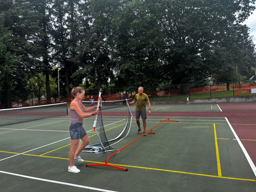 Camas residents Dawn, left, and John Hendricks, of Camas, set up a pickleball net on the shared-use tennis-pickleball courts at Crown Park in Camas, Aug. 12, 2024.