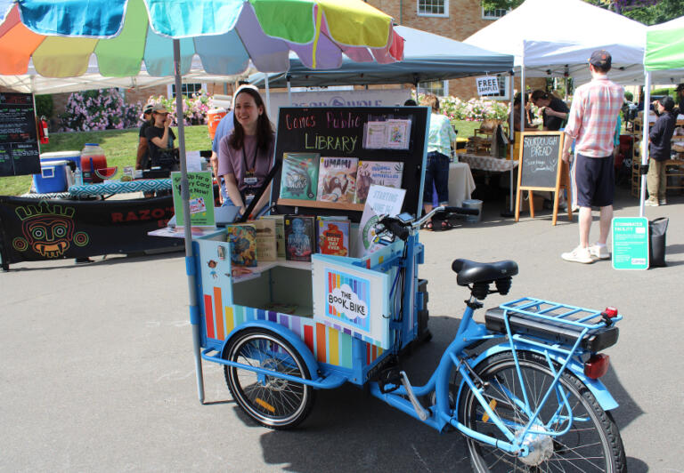 Maria Martin, a library associate at the Camas Public Library, staffs the library&rsquo;s Book Bike, a mobile lending library, at the Camas Farmer&rsquo;s Market in downtown Camas on Wednesday, June 11, 2025.