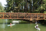 Paddleboarders wait as kids jump off a bridge into Round Lake on June 24 in Camas. (Taylor Balkom/The Columbian files)