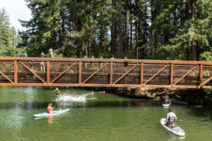 Paddleboarders wait as kids jump off a bridge into Round Lake on June 24 in Camas. (Taylor Balkom/The Columbian files)