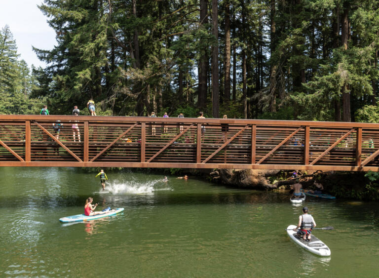 Paddleboarders wait as kids jump off the Everett Street footbridge into Round Lake on June 24 in Camas.