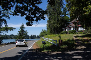 A motorist passes Lacamas Lake, left, while driving past the Leadbetter House, right, on Northeast Leadbetter Road in Camas on July 1. The Leadbetter Walk & Roll event will close Leadbetter Road to motorized vehicles from the city’s boat launch to Camp Currie from 1-4 p.m. Sept. 14 to give pedestrians and bicyclists safe access to the roadway and to explore two of the city’s Legacy Lands properties. (Amanda Cowan/The Columbian)