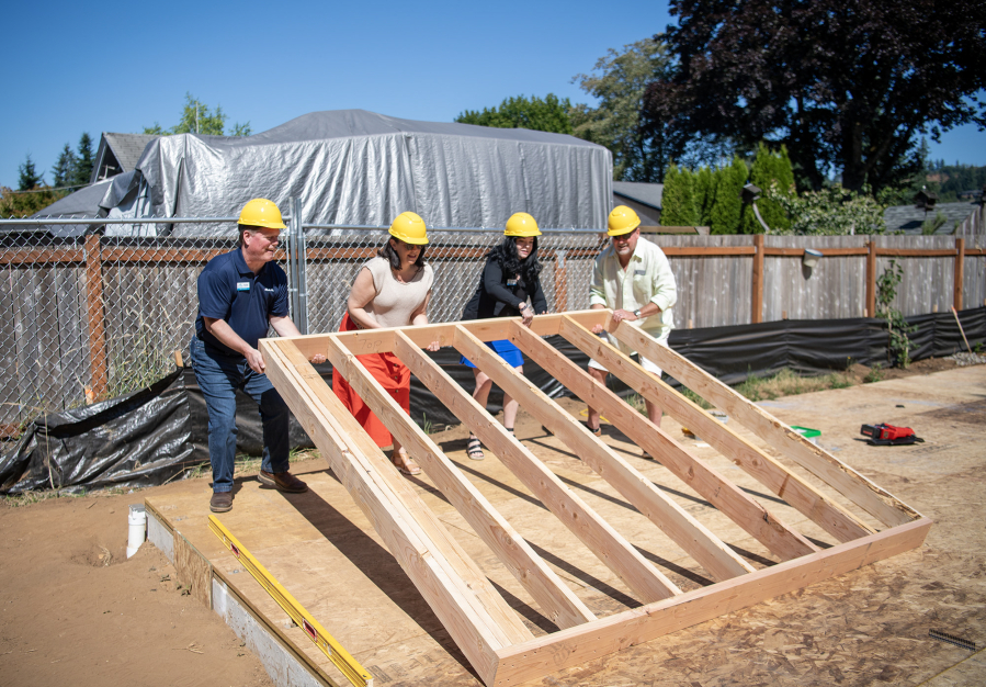 Camas-Washougal Chamber of Commerce board member Ken Cline, from left, administrator Samantha Horner, executive director Jennifer Senescu and Washougal Mayor David Stuebe lift the first section of wall on a house Friday, July 11, in Washougal. The single-family, four-bedroom house is the first built in Washougal by Evergreen Habitat For Humanity. (Taylor Balkom/The Columbian)