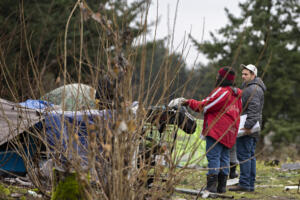 Council for the Homeless outreach team members Magellan Rankin, in maroon, and Brian Starbuck offer supplies to a man at an encampment near Interstate 205 on Jan. 25, 2024, while conducting the Point-in-Time Count. In 2025, the annual survey showed a 12 percent increase in people experiencing some form of homelessness in Clark County. (Amanda Cowan/The Columbian files)