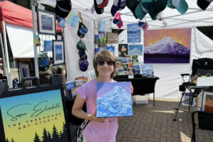 Washougal resident Rachel Foote holds a painting of Mount Hood, created by Washougal artist Susan Fronckowiak, during the 2024 Washougal Arts and Music Festival on Aug. 10, 2024.