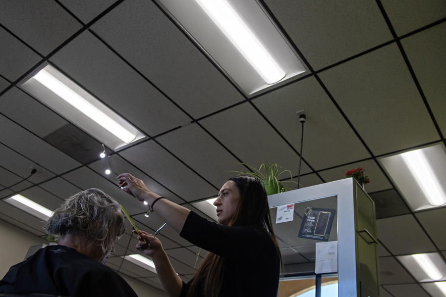 Overhead lights illuminate Ruth Mougey of Vancouver, left, as she joins Jenifer Orsini of Utopia Salon on Tuesday afternoon. Utopia Salon is one of the local businesses that has recently used Clark Public Utilities incentives&rsquo; to install new lights to lower electricity use. (Amanda Cowan/The Columbian)
