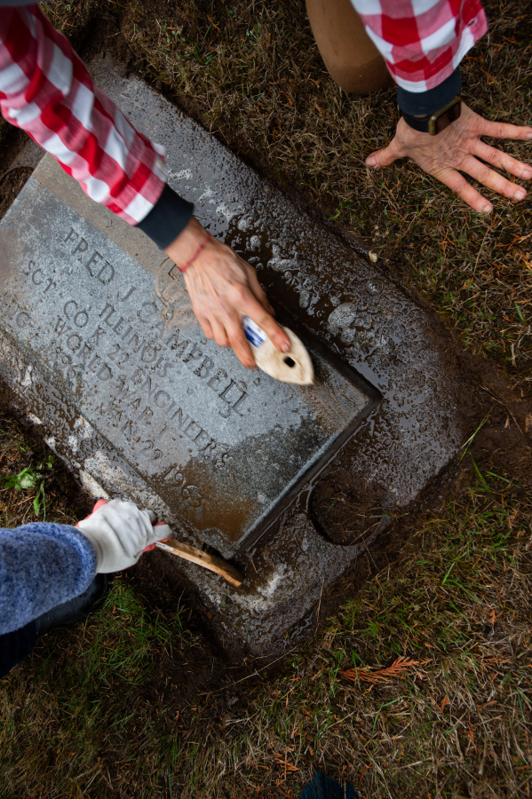 The grave marker of World War I veteran Fred J. Campbell gets a good scrubbing during a recent work party at Brush Prairie Cemetery. (James Rexroad/for The Columbian)
