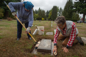 Katherine MacArthur-Krall, left, and Lorie Hoffman scrub the grave marker for Sgt. Fred Campbell, a World War II veteran, at Brush Prairie Cemetery during a recent work party. (James Rexroad for The Columbian)