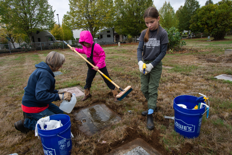 Fort Vancouver chapter of the Daughters of the American Revolution&rsquo;s cemetery committee member Ruth Morgan works to clean veterans&rsquo; grave markers at Brush Prairie Cemetery with her granddaughters, Sarah Liou, center, and Cora Liou, right. (Photos by James Rexroad for The Columbian)