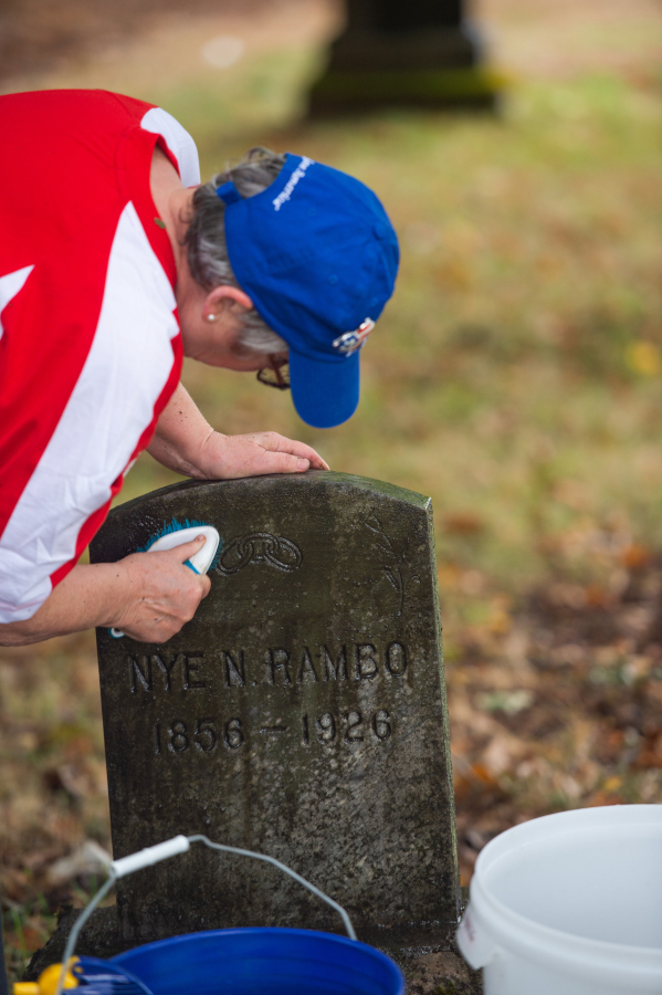 Fort Vancouver chapter of the Daughters of the American Revolution&rsquo;s cemetery committee member Peri Muhich scrubs the headstone of a World War I veteran named Nye N. Rambo at Brush Prairie Cemetery. (James Rexroad for The Columbian)