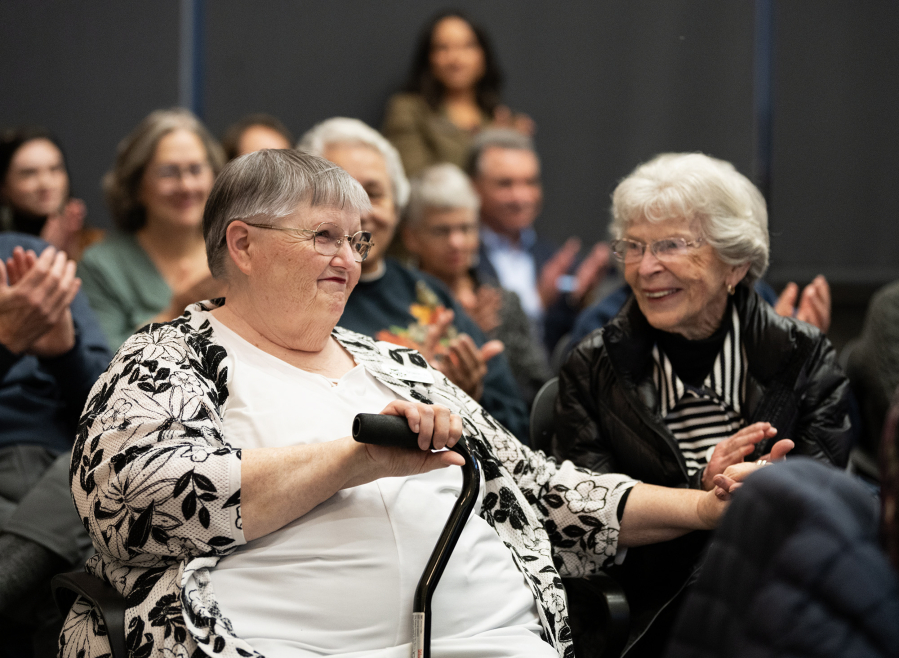 Sharon Wodtke, left, smiles as she holds her sister Patti Taylor&rsquo;s hand and applause breaks out Wednesday during a Clark County Commission on Aging meeting at the Clark County Public Service Center. Wodtke, a Battle Ground resident, received the commission&rsquo;s sixth annual Silver Citizen Award. (Taylor Balkom/The Columbian)
