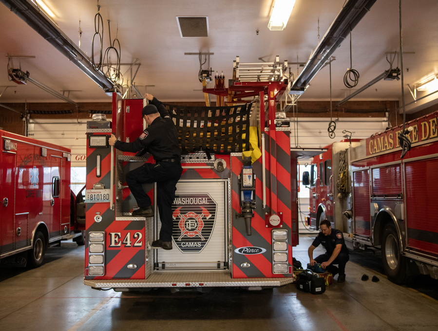 Firefighter paramedic Bailey Duncan, left, climbs down the back of an engine while fellow firefighter paramedic Nate Barmore works with equipment on the ground March 21 at Camas Fire Station 42. (Taylor Balkom/The Columbian files)