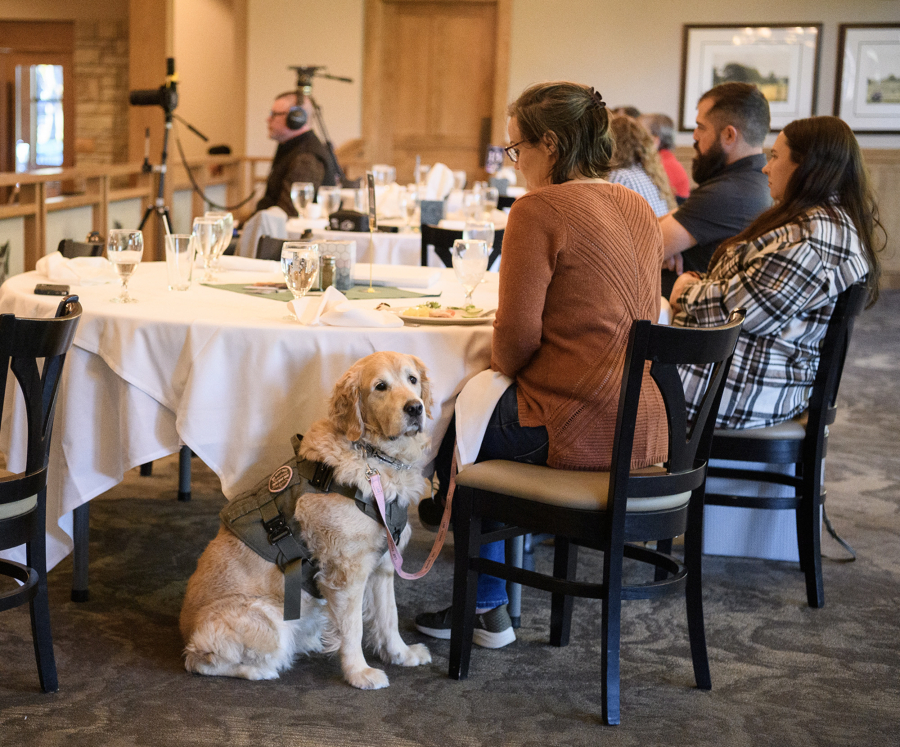 Service dog Diamond, center, sits next to handler and veteran Dodi Lewis on Friday during a Northwest Battle Buddies graduation ceremony at Royal Oaks Country Club in Vancouver. (Taylor Balkom/The Columbian)