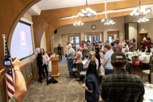 A room stands and applauds as Northwest Battle Buddies’ 300th service dog, Missy, at left, is given to a veteran Friday during a Northwest Battle Buddies graduation ceremony at Royal Oaks Country Club in Vancouver. (Taylor Balkom/The Columbian)