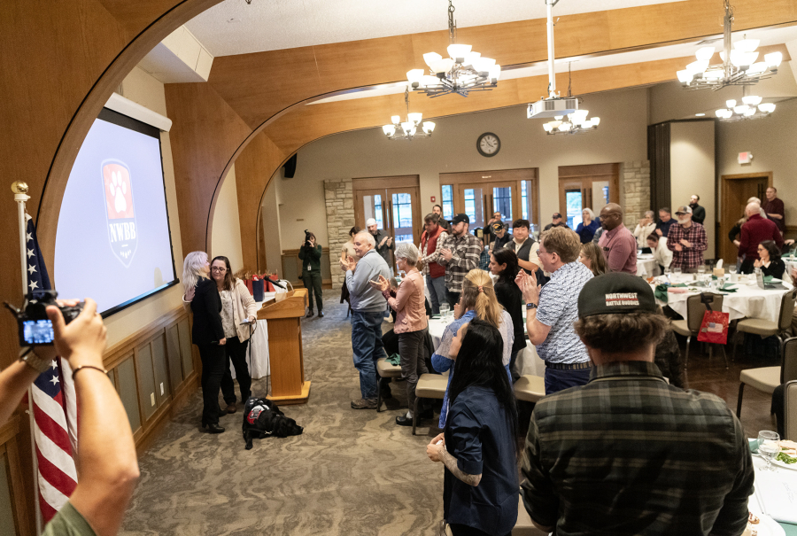 A room stands and applauds as Northwest Battle Buddies&rsquo; 300th service dog, Missy, at left, is given to a veteran Friday during a Northwest Battle Buddies graduation ceremony at Royal Oaks Country Club in Vancouver. (Taylor Balkom/The Columbian)