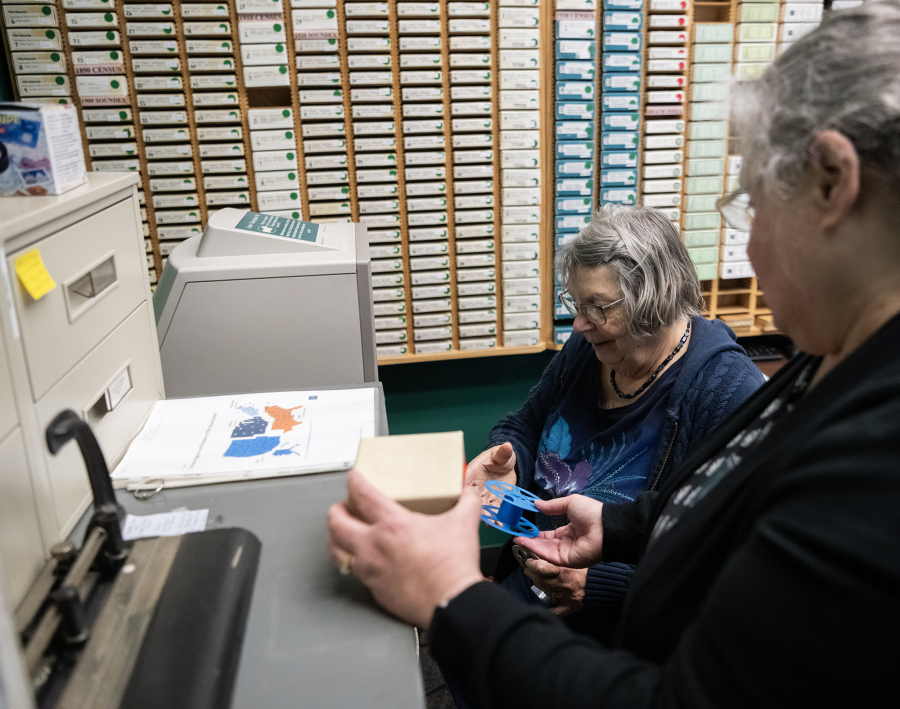 Clark County Genealogical Society member Jane Germann, center, works to put a Lacamas News microfilm reel into a projector Friday at Clark County Genealogical Society. The Camas Public Library recently donated its historical newspaper microfilm collection to the organization. (Taylor Balkom/The Columbian)