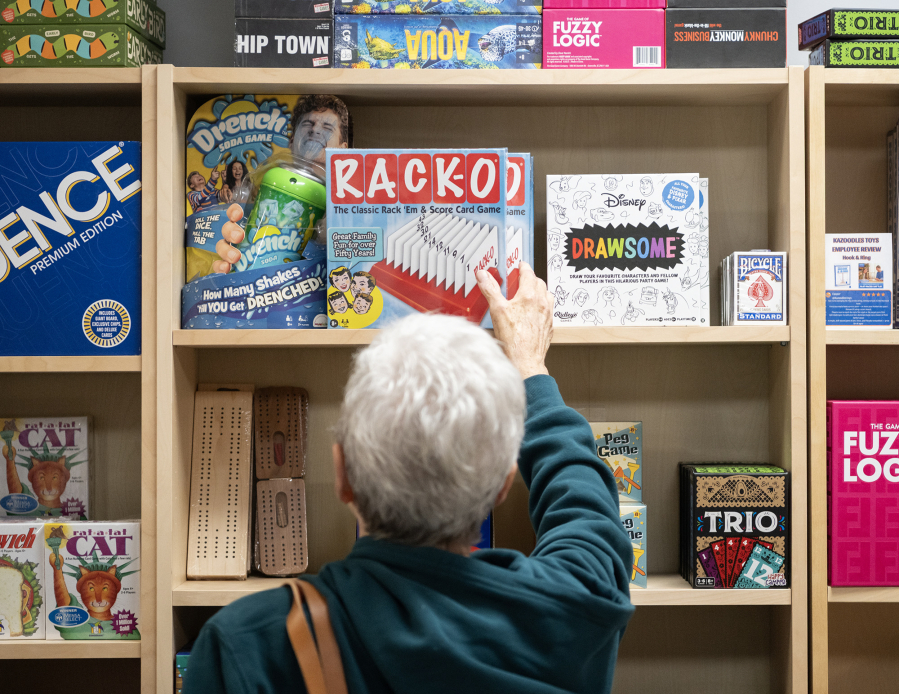 Diana Smith of Vancouver examines a wall of games Thursday at Kazoodles Toys & Gifts in east Vancouver. (Taylor Balkom/The Columbian)