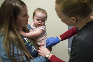 Tamine Robinson of Battle Ground, left, holds her daughter Riley, 1, as registered nurse Julie Ward administers the measles-mumps-rubella vaccine at Legacy Medical Group in Vancouver on March 1, 2019. (The Columbian files)