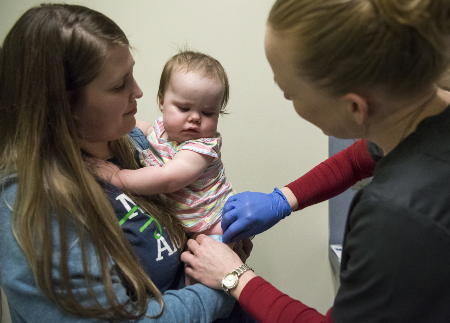 Tamine Robinson of Battle Ground, left, holds her daughter Riley, 1, as registered nurse Julie Ward administers the measles-mumps-rubella vaccine at Legacy Medical Group in Vancouver on March 1, 2019. (The Columbian files)