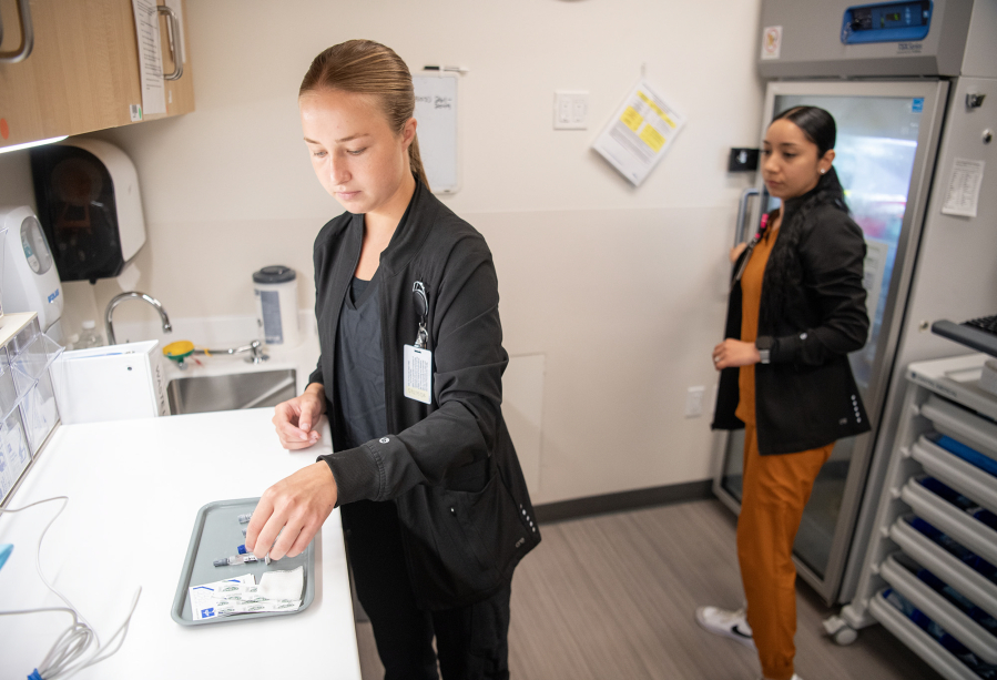 Student medical assistant Megan Kivari, left, places vaccines on a tray under the supervision of mentor Miriam Castro-Vega on July 23 at Kaiser Cascade Park Medical in Vancouver. (Taylor Balkom/The Columbian files)