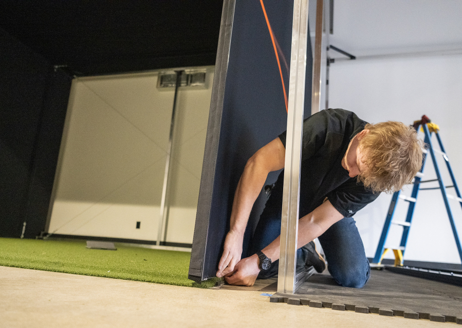 Trackman worker Dominic Miller installs one of two indoor golf simulators Tuesday at Camas Indoor Golf Club in Camas. (Taylor Balkom/The Columbian)