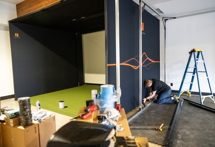 Trackman worker Dominic Miller installs one of two indoor golf simulators Tuesday at Camas Indoor Golf Club in Camas. (Taylor Balkom/The Columbian)