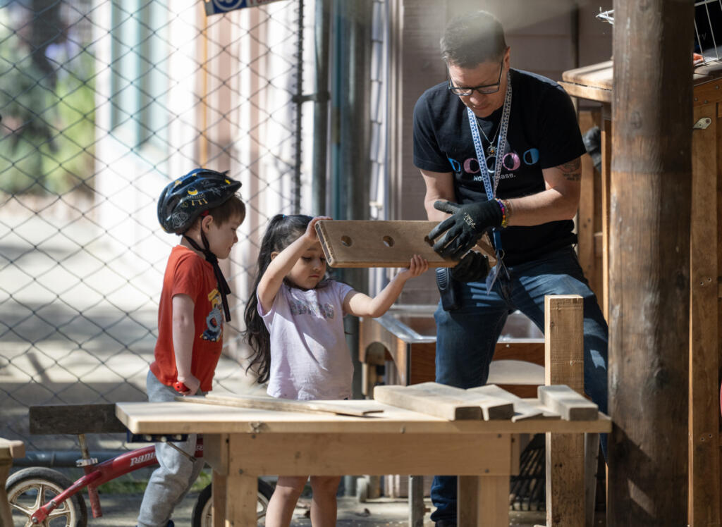 Outdoor area preschool teacher Matthew Philbrook, right, puts pieces of wood away with students Arielle Herrera, center, and Miles Hess on Thursday morning at the Clark College child care center and lab school in the Child and Family Studies area. (Taylor Balkom/The Columbian)